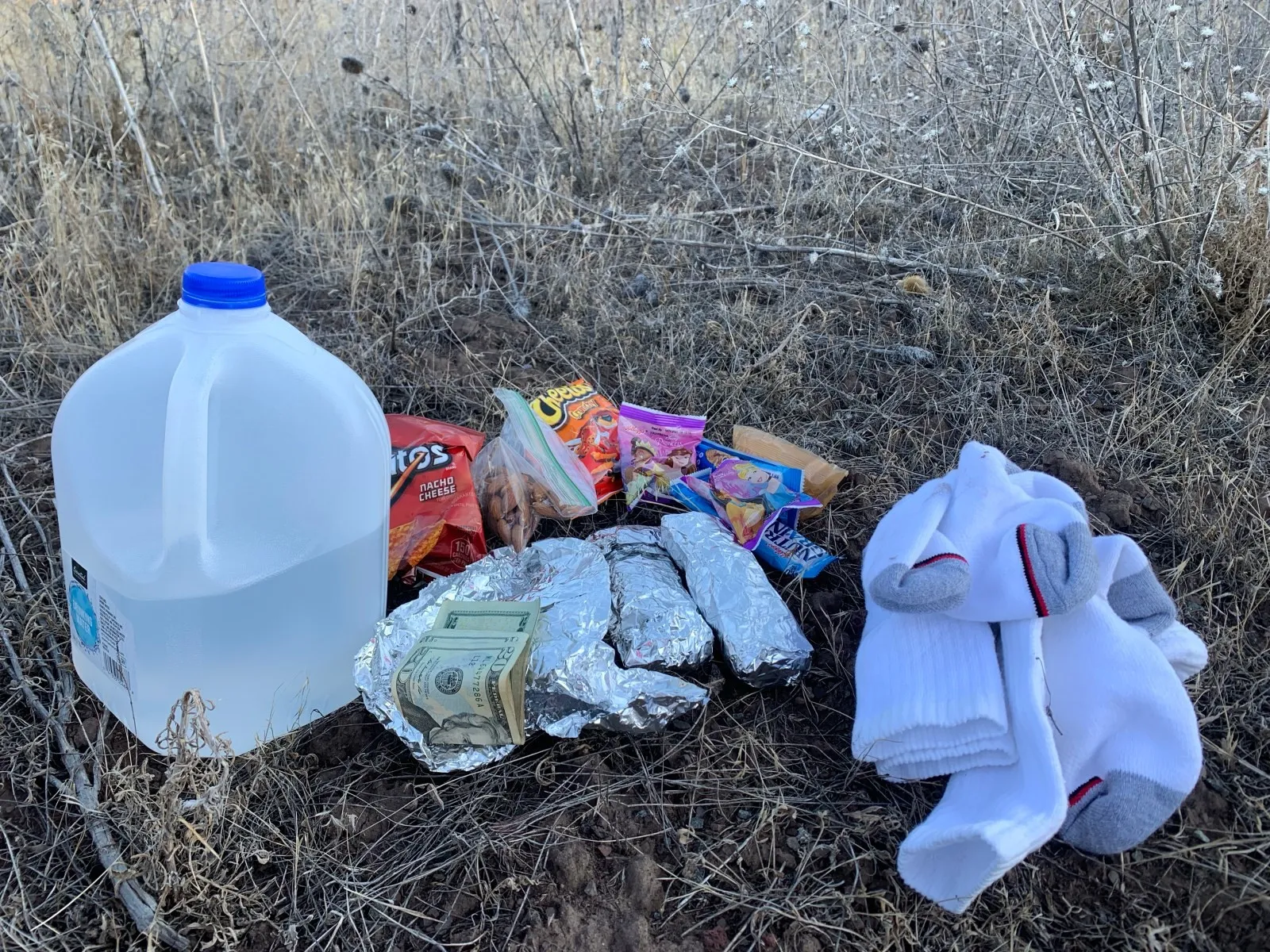 A gallon of water, snacks and fresh socks laid out on dry grass