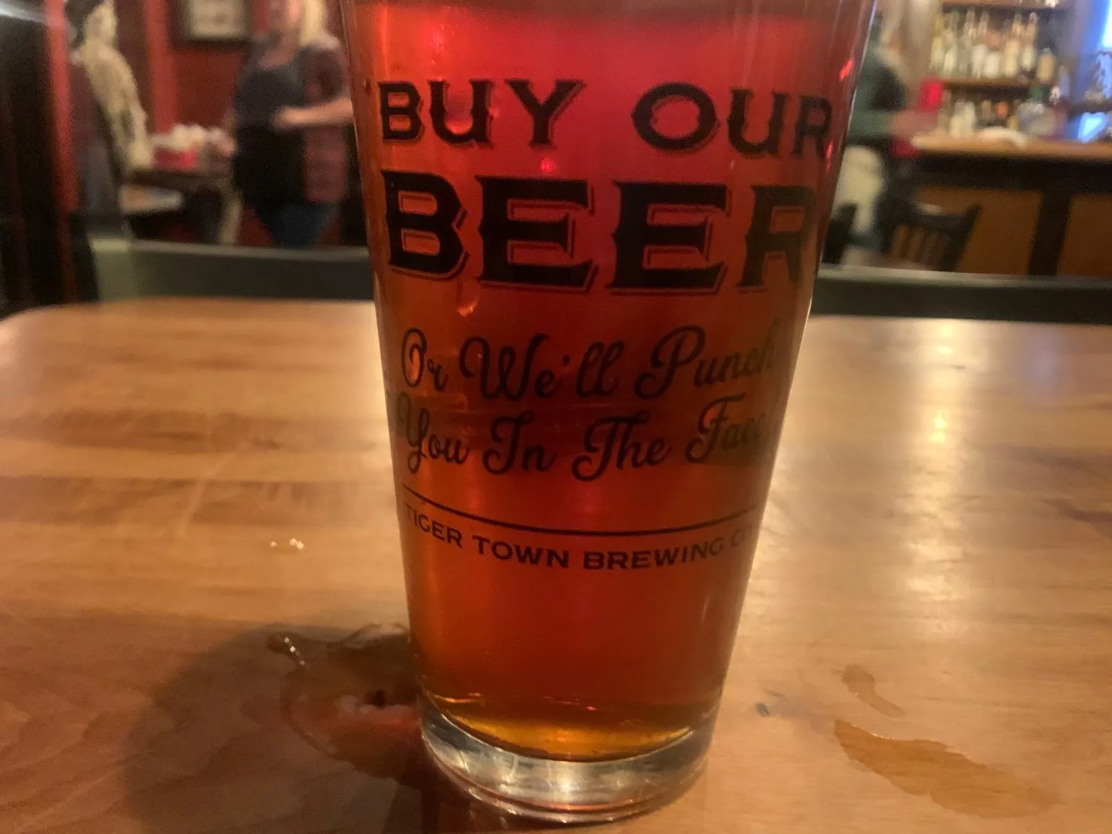 A pint glass printed “Buy our beer” on a bar table
